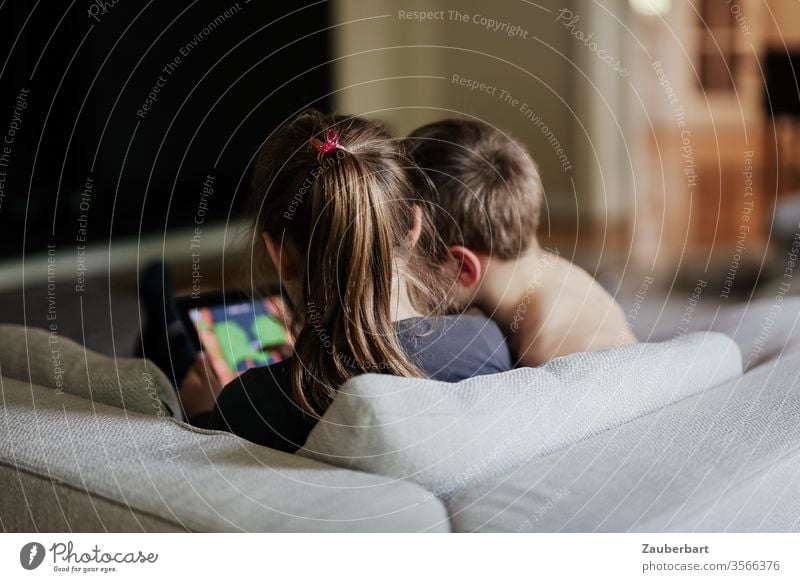 Die Köpfe zweier Kinder, die mit Tablet-Computer auf dem Sofa spielen Kindheit Spielen Tablet Computer Wohnung zuhause Junge Mädchen Pferdeschwanz Kissen