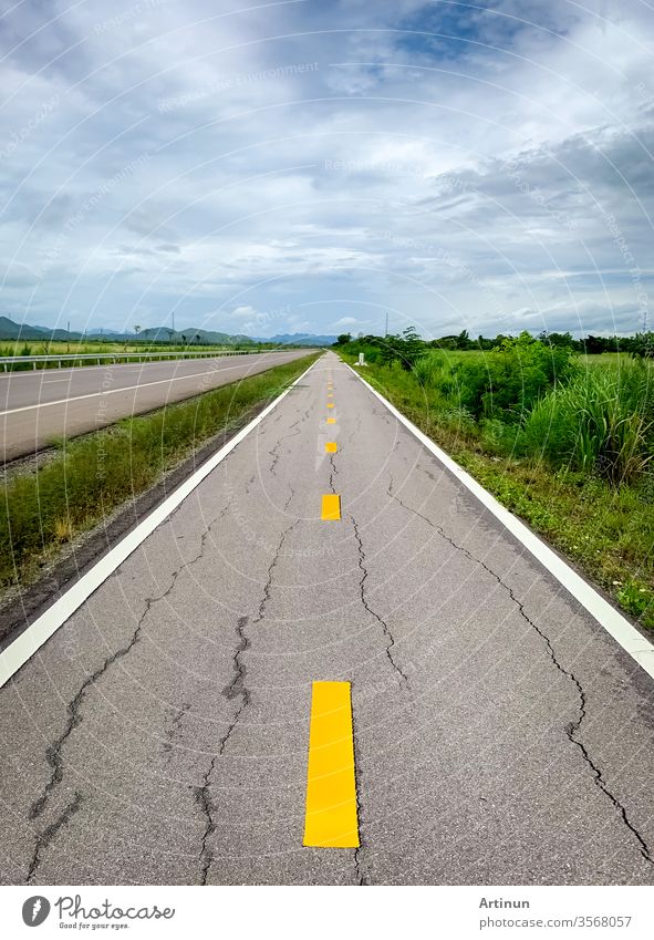 Perspektivisch gerissene Asphaltstraße vor dem Berg. Lange gerade beschädigte Asphaltstraße. Schlechter Belag des Radweges und weißer Himmel und Wolken mit grünem Gras neben der leeren Straße. Naturlandschaft.