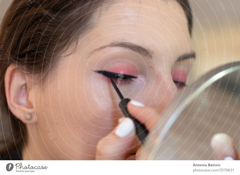 Nahaufnahme einer erwachsenen Brünetten beim Auftragen von Eyeliner auf sich selbst, Augen geschlossen, während sie Katzenaugen erzeugt Gesundheit Wimpern