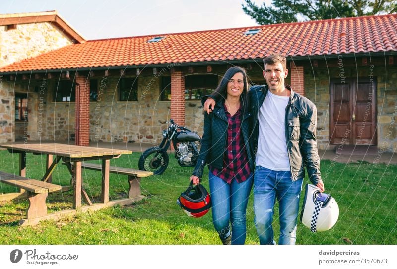 Paar zu Fuß umarmt und benutzerdefiniertes Motorrad attraktiv jung laufen altehrwürdig Haus Picknick-Tisch Fahrrad retro Fahrzeug Biker Verkehr Mode Freundin