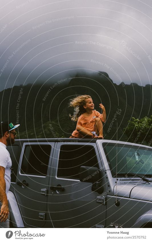 Kind sitzt auf einem Autodach und der Wind weht ihr das Haar zurück Hawaii Sturm Strand Himmel Küste Wolken Farbfoto Natur Außenaufnahme Landschaft Unwetter