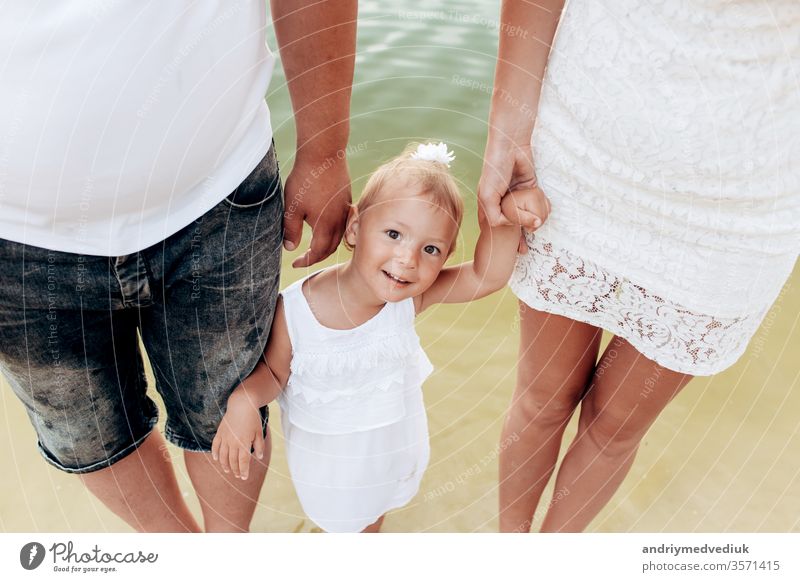 Mama, Papa, Tochter gehen auf Steinen in der Nähe des Sees. Blick nach unten. Ansicht von unten auf die Beine. Das Konzept der Sommerferien. Mutter-, Vater- und Babytag. Die Familie verbringt gemeinsam Zeit in der Natur. Blick der Familie.