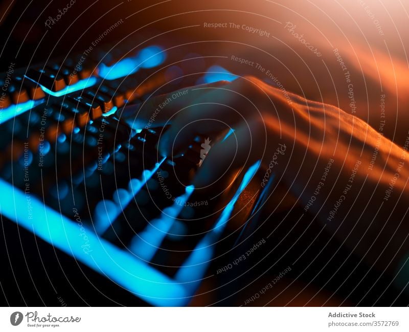 Crop-Programmierer tippt auf einer Tastatur mit blauer Hintergrundbeleuchtung in einem dunklen Raum zu Hause Keyboard Rücklicht Tippen Nacht Hand Mann Komfort