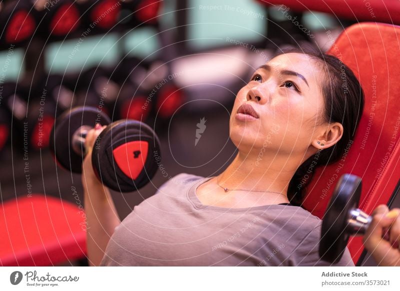 Starke ethnische Sportlerin trainiert mit Hanteln auf Bank in moderner Turnhalle Frau Fitness Kurzhantel Presse Truhe Training Steigung Übung Athlet