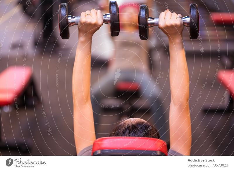 Anonyme starke ethnische Sportlerin trainiert mit Hanteln auf der Bank in moderner Turnhalle Frau Fitness Kurzhantel Presse Truhe Arme hoch Training Steigung