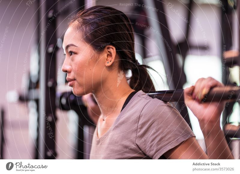 Kräftige junge asiatische Sportlerin macht Kniebeuge mit Langhantel in moderner Turnhalle Frau Curl-Hantel Training aktive Kleidung Maschine Gerät Fokus atmen