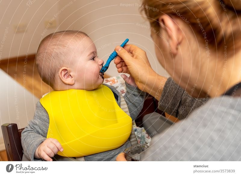 Entzückender kleiner Junge im Fütterungsstuhl, der von seiner Mutter mit einem Löffel gefüttert wird Baby niedlich Europäer Säugling 6 Monate Kaukasier