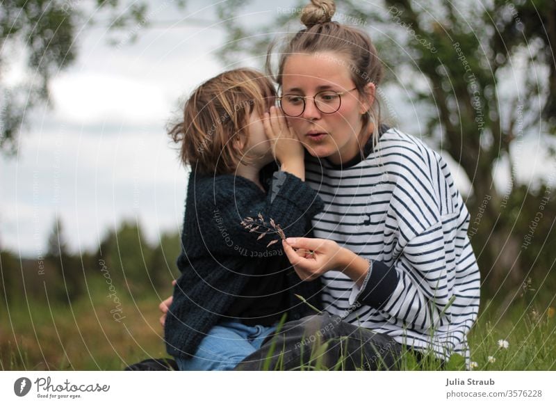 Mädchen flüstert Frau mit Brille etwas ins Ohr hören zuhören Flüstern Wiese Blume Wald gestreift gestrickt blau weiß grün Brillenträger Hipster Dutt Kind