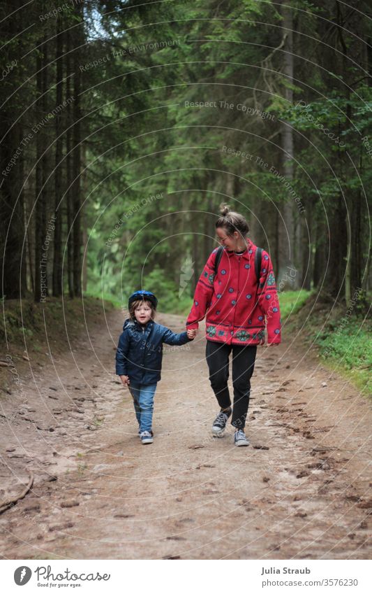 Frau läuft mit Kind spazieren im Wald Waldweg Erde Tannenzapfen Bäume Fichtenwald Fahrradhelm wandern laufen Dutt fleecejacke Regenjacke Chucks gemeinsam