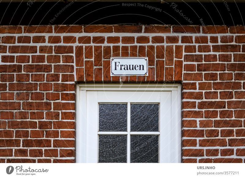 Frauen als Schriftzug auf einem Emaileschild über einer Glastür an einer Backsteinwand Tür Fenster Toilette Toilettenschild menschenleer Farbfoto alt Mauer