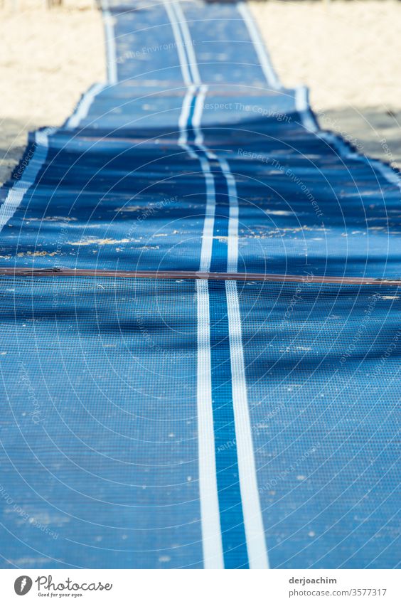 Ausgerollt. Langer blauer Läufer mit weißen Streifen, mit Falten, liegt am Srand zum Zugang zum Meer nur für Behinderte.. Teppich Läufer Bodenbelag