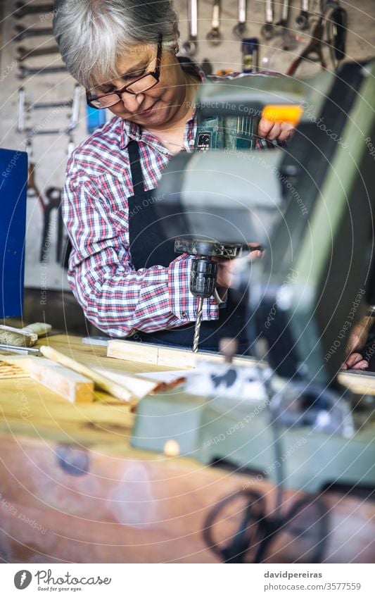 Ältere Frau in einer Tischlerei Senior Zimmerer Handwerkerin Werkstatt bohren arbeiten Holz reif Business Kaukasier heimwärts Schreinerei Ruhestand Arbeiter