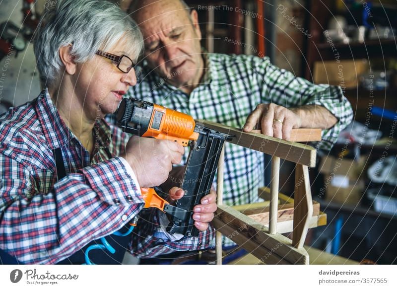 Seniorenpaar in einer Tischlerei Schreinerei Frau Kunstgewerbler Tacker Nagelspitzen Zusammenbau Stuhl diy Zimmerer Paar Möbel Werkstatt arbeiten Holz reif