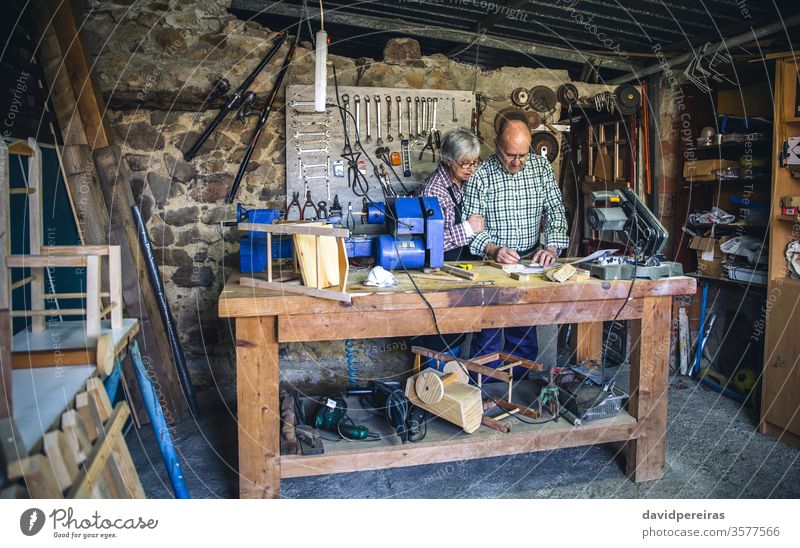 Seniorenpaar in einer Tischlerei Werkstatt Schreinerei Werkbank Paar Maßnahmen Markierung arbeiten Zimmerer Holz reif Maschine Business Kaukasier Stuhl