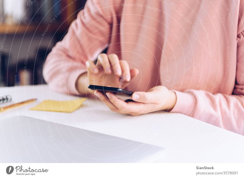 Junge Frau benutzt ein Mobiltelefon, während sie zu Hause mit einem Laptop arbeitet. Business heimwärts Technik & Technologie klug Telefon Computer Schreibtisch