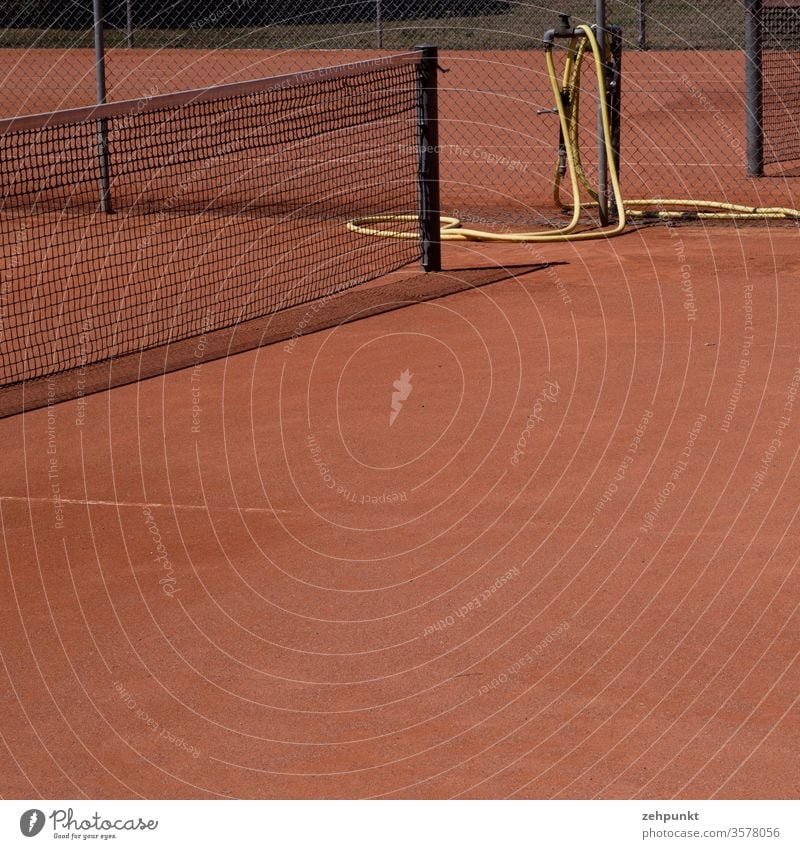 Ausschnitt von einem Tennisplatz mit Teilen des Netzen, rotem Sand, gelbem Wasserschlauch, schmaler Schattenwurf des Netzes schwarz Leerraum Menschenleer Sport