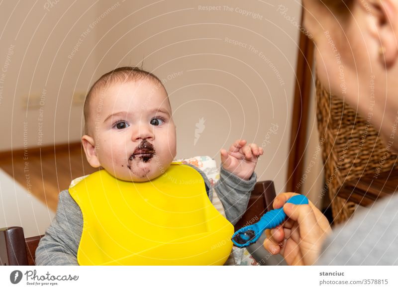 Entzückender kleiner Junge im Fütterungsstuhl, der von seiner Mutter mit einem Löffel gefüttert wird Baby niedlich Europäer Säugling 6 Monate Kaukasier