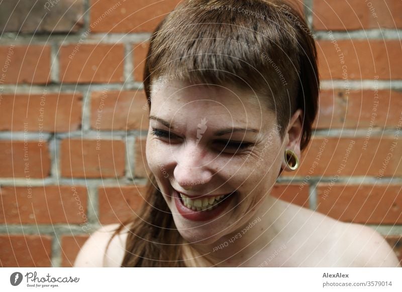 Portrait einer lachenden, jungen Frau vor einer Backsteinwand Spaß frei wild Freude heiter zuversichtlich Vertrauen Textfreiraum rechts Coolness