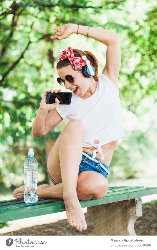 Junge Frau hört die Musik auf ihrem Smartphone im Park jung Glück hören WiFi Lifestyle genießend Spaß freudig Gesang Frühling Sommer niedlich schön modern