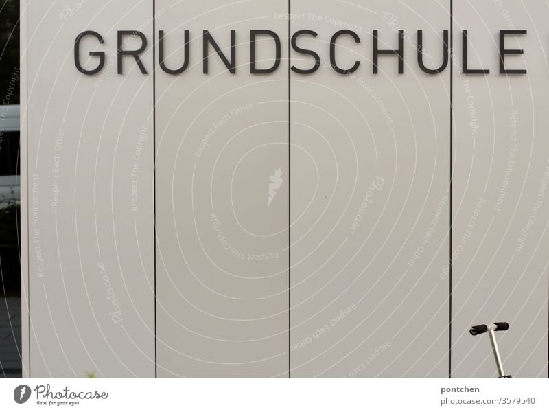 Das Wort Grundschule steht auf einer Fassade. Vor dem Gebäude steht ein roller.  Bildung. schild wort schulsystem bildung schulanfang lernen Kindheit Schulkind