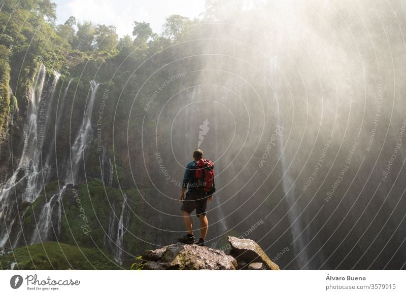 Ein rucksackreisender Abenteurer blickt voller Ehrfurcht auf den gewaltigen Felsenzirkus, der von den gewaltigen Wasserfällen bei Tumpak Sewu in Ostjava, Indonesien, gebildet wird.