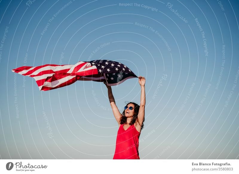 junge Frau, die bei Sonnenuntergang die Flagge der Vereinigten Staaten im Freien hält. Unabhängigkeitstag in Amerika, Konzept des 4. Juli Vereinigte Staaten