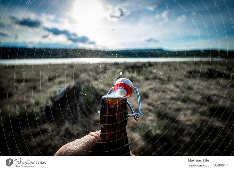 Genießt das Leben. Prost! Flasche Flaschenhals Bierflasche Bügelverschluss Büro Sonne Gegenlicht See Bierchen trinken Getränk Glasflasche Hand öffnen Biergarten