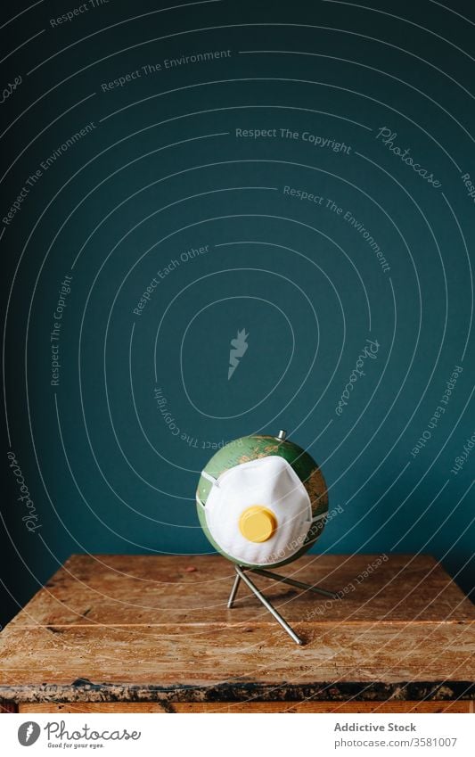 Kleiner Globus mit Atemschutzmaske auf dem Schreibtisch wenig Pandemie Atemschutzgerät Mundschutz Bund 19 COVID19 Coronavirus behüten Konzept kreativ Model