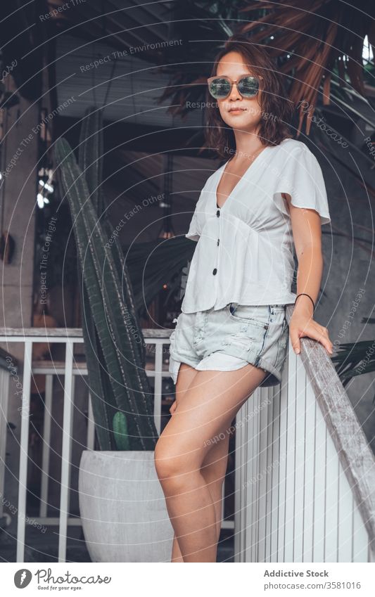 Selbstbewusste junge Frau mit Sonnenbrille auf der Terrasse gegen exotische Pflanzen im Hotel selbstbewusst Lächeln Tourismus Loft Smartphone cool tropisch Bali