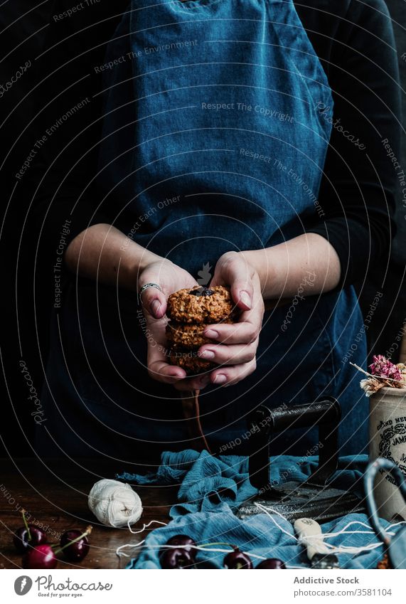 Kornhausfrau mit hausgemachten Keksen mit Kirsche selbstgemacht Stapel frisch Schürze Hausfrau Tisch Küche Haufen dunkel Frau Haferflocken Knusprig