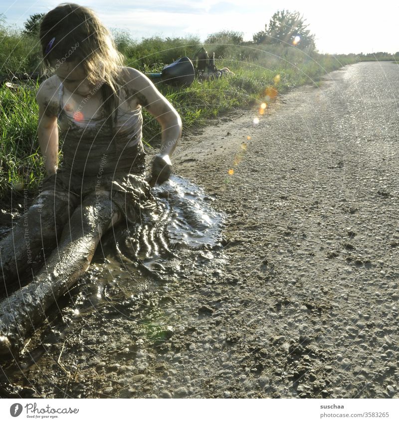 kind sitzt an einem wegesrand im matsch und schmiert sich von unten bis oben ein damit Kind Kindheit Freiheit auf dem Lande Landschaft Sommer draußen Weg