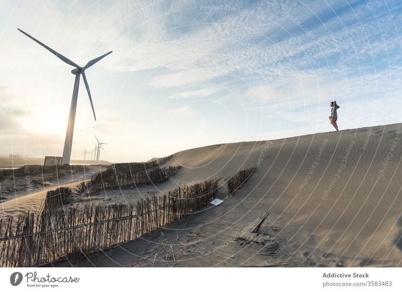 Unbekannter Reisender steht bei Sonnenuntergang auf Sandhügel nahe Windmühle Himmel Hügel Horizont Harmonie Landschaft malerisch Hügelseite erkunden Skyline