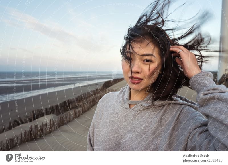 Junge Asiatin steht bei windigem Wetter am Meeresstrand Frau MEER Strand Skyline Harmonie Sand Haare berühren Küste nachdenklich reflektierend Windstille