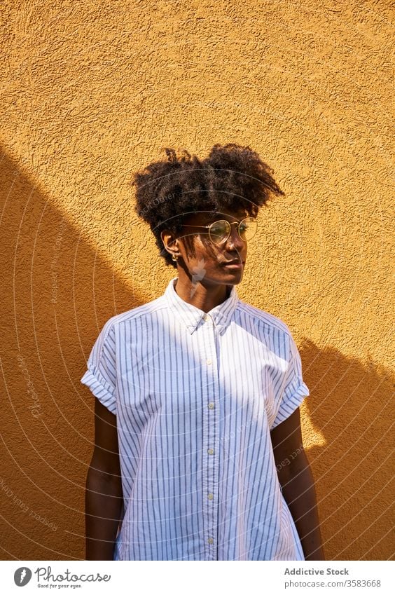 Stilvolle, nachdenkliche schwarze Frau an einem sonnigen Tag auf der Straße Persönlichkeit trendy farbenfroh Afro-Look ruhig besinnlich Brille Windstille