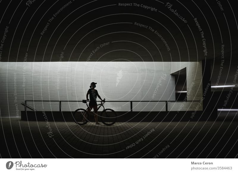 die Silhouette einer Person, die ihr Fahrrad durch die Straßen der Stadt schiebt eine Person gebaute Struktur Kontrast Architektur Stadtstraße Seitenansicht