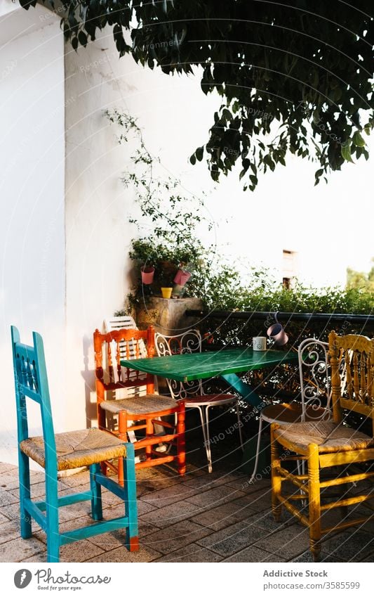 Malerischer Tisch mit Stühlen auf Terrasse mit Grünpflanzen Landschaft Haus Veranda farbenfroh Stuhl Metall Zaun Efeu heimwärts Cottage Gebäude Außenseite