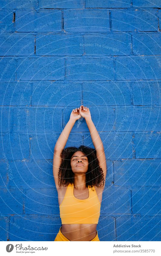 Verträumte afroamerikanische Frau, die sich auf der Straße an eine Wand lehnt verträumt Wachtraum Afro-Look Farbe lebhaft pulsierend ruhig Steinwand ethnisch