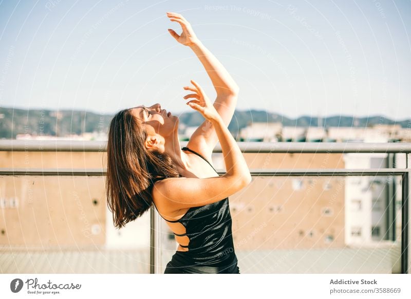 Gelassene Frau tanzt auf der Terrasse Tanzen Anmut Tänzer Gelassenheit ausführen Sommer ruhig beweglich Handfläche Baum urban jung aufschauend Windstille