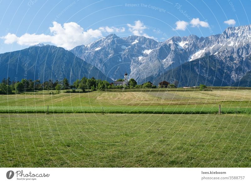 Grüne Wiesen entlang der felsigen Bergkette mit typisch österreichischer Kleinkirche, Mieming, Österreich Landschaft Berge Himmel Natur Sommer mieming grün