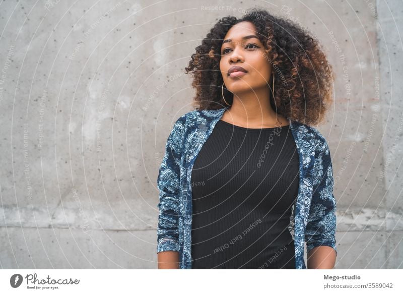 Afroamerikanische Frau gegen graue Wand. Afro-Look jung Mädchen Gesicht Ausdruck Erwachsener Blick Mode schwarz Stehen Lächeln selbstbewusst Behaarung brünett