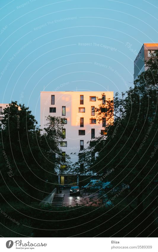 Ein von der Sonne angestrahltes Hochhaus am Abend und ein Auto das in eine Tiefgarage fährt. Wohnhaus Sonnenstrahlen Abenddämmerung Wohngegend Sonnenschein