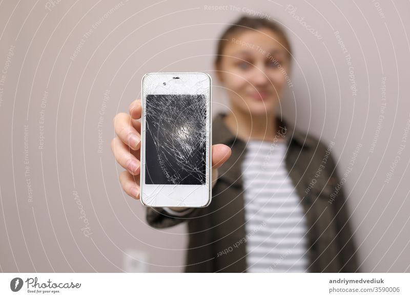 Frustrierte junge Frau hält Handy mit zerbrochenem Bildschirmglas in der Hand. Das Display des Telefons muss repariert werden. Isoliert auf grauem Hintergrund. selektiver Fokus auf Smartphone