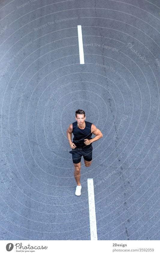 Draufsicht auf einen Athleten, der in schwarzer Sportkleidung auf der Straße trainiert. Mann Erwachsener Joggen Lifestyle sportlich Läufer Übung jung aktiv