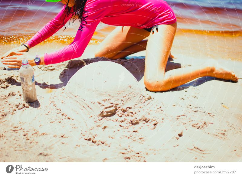 Im heißen Sand soll ein Australia Schneemann gebaut werden. Eim Mädchen im roten Badeanzug am Wasser hat schon einen kleinen runden Hügel geformt. Sommer Strand