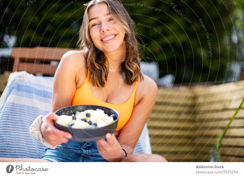 Lächelnde Frau mit Schale mit frischen Früchten Frucht Schalen & Schüsseln Sommer Kälte Beeren Liegestuhl Terrasse heiter sich[Akk] entspannen ruhen sitzen reif