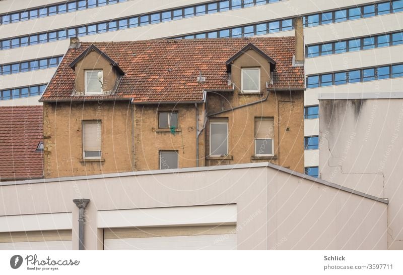 Altes Wohnhaus mit Ziegeldach eingeklemmt zwischen Garagen und Bürogebäude Haus alt Dach Mauer sauber Schatten Straßenlampe Hochhaus Gegensatz alt und neu