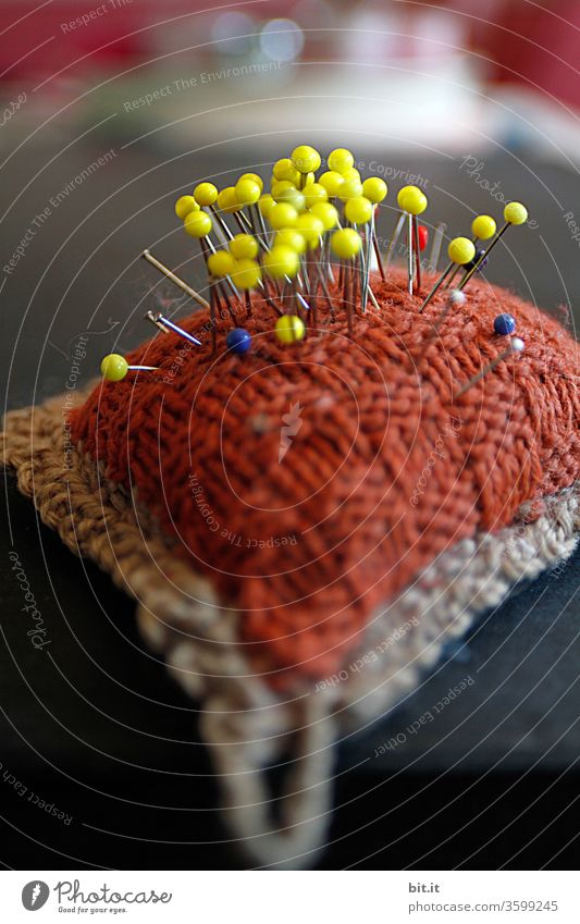 alt l altes, nostalgisches, gestricktes, selbstgemachtes Nadelkissen aus Wolle mit Nadeln bespickt. Viele gelbe Stecknadeln stecken zusammen im Retro-Nadelkissen. Schneiderei, Werkstatt, Bastelraum, Nähtisch, Hobbyraum, Heimwerken, Nähkurs & Nähutensilie.