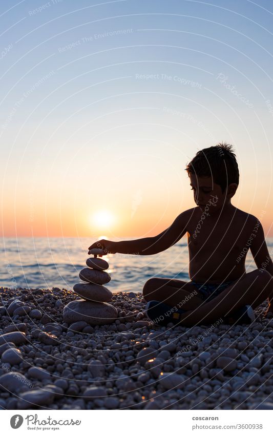 Kleines Kind spielt mit Steinen am Strand bei Sonnenuntergang Aktivität Hintergrund Gleichgewicht Ausgewogenheit schön Schönheit Junge Kindheit Textfreiraum