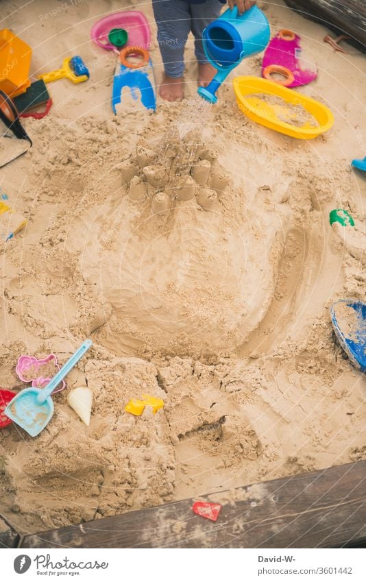 Kind spielt im Sandkasten Spielzeug Spaß Freude selbstbeschäftigung anonym gießen Wasser nass Gießkanne sandig garten Spielplatz Spielen Außenaufnahme Kleinkind