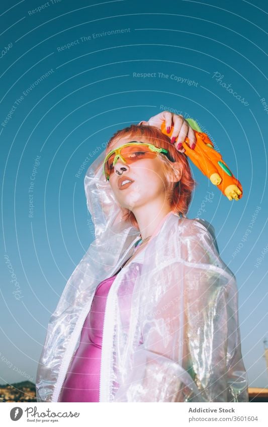 Retro-futuristische Frau mit Wasserpistole schaut in die Kamera Pistole Erfolg Arm angehoben Himmel Stil jung retro schreien Outfit Model gefärbtes Haar trendy